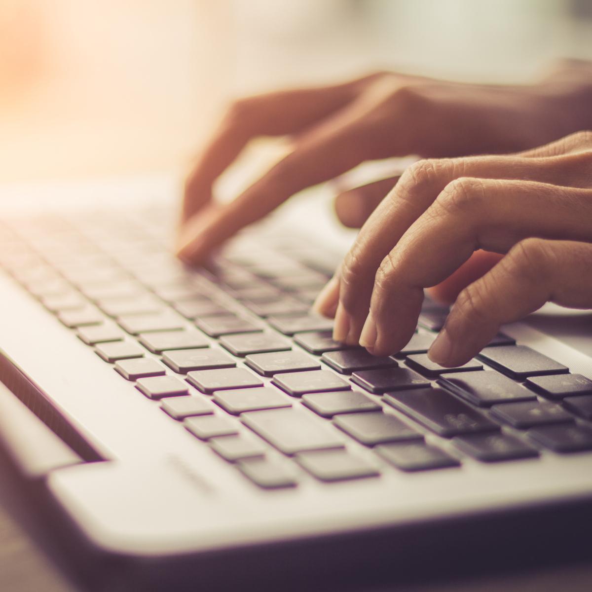 Eine Person an ihrem Laptop sitzt und in die Tasten tippt.